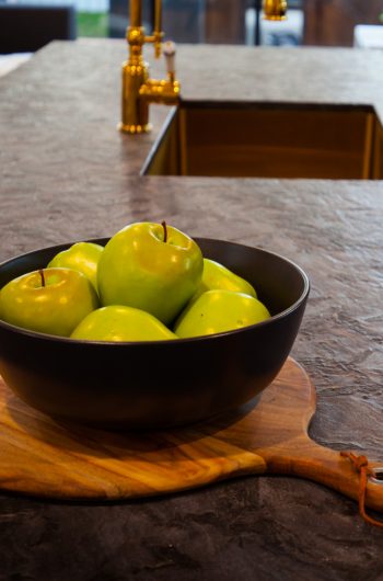 kuchnia z kamienia naturalnego w kolorze czarnym, na środku miska z zielonymi jabłkami