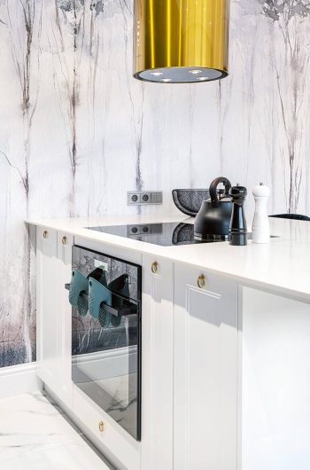 Wyspa w kuchni ze spieku kwarcowego Marazzi ''Statuario'' lux. Nad wyspą złoty w kształcie tuby okap.