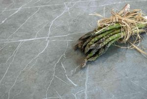 Zdjęcie przedstawia pęczek zielonych szparagów przewiązany naturalnym sznurkiem z rafii, spoczywający na blacie wykonanym ze spieku kwarcowego Neolith. 