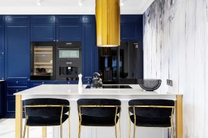 Na grafice widzimy nowoczesną, luksusową kuchnię o odważnym i eleganckim designie, z dominującymi akcentami w kolorze granatowym, złotym i białym.